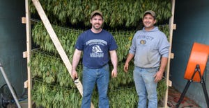 Chris and Bryan Harnish stand in front of homemade racks hanging with premium hemp buds