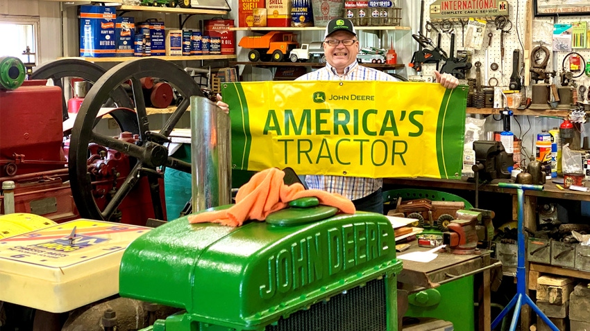 man holds America's Tractor sign in workshop