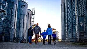 A family with young children walking between a grain storage facility