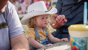 A young girl in a cowboy hat being spoon fed ice cream