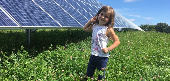  young girl  posing in field of red, white, crimson, and ladino clover with solar panel in background
