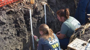  Two young ladies in a pit of soil as they take measurements 