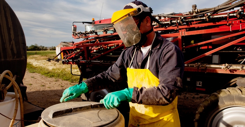 farmer wearing protective mask, apron and gloves while removing lid of chemical container on a farm
