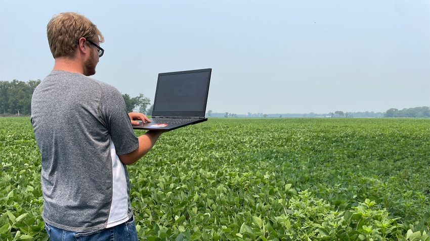 A man working on a laptop computer as he stands in a field