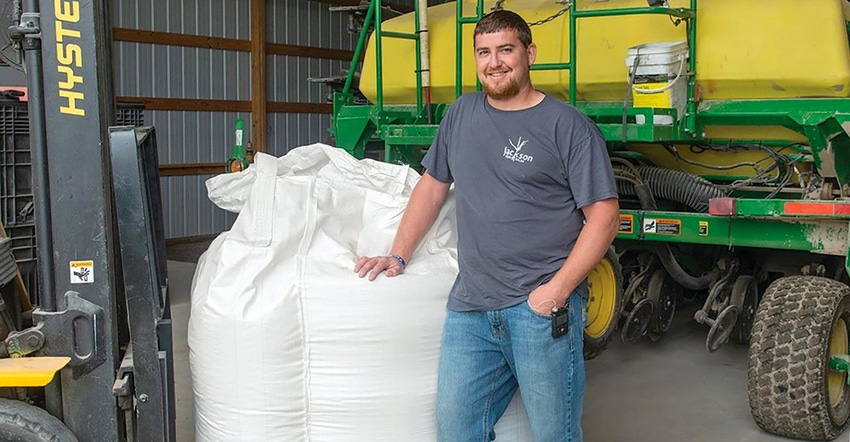 Farmer Michael Jackson standing in front of a John Deere tractor and leaning on a white bag of seed