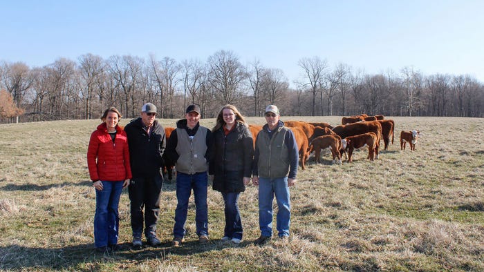 A group of people pose in front of cattle grazing in a field