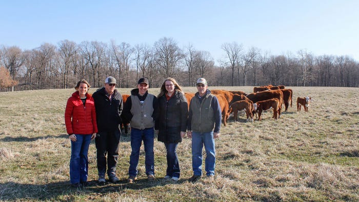 A group of people pose in front of cattle grazing in a field A group of people pose in front of cattle grazing in a field