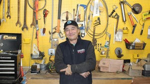 Howard Prussack stands in front of yellow pegboard where he hangs his tools