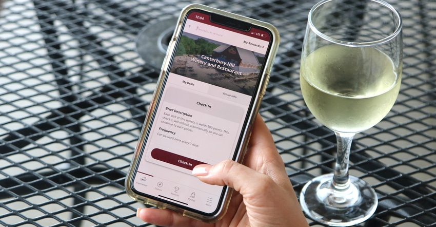 Hand holding smartphone while using an app with a table and wine glass in the background Hand holding smartphone while using an app with a table and wine glass in the background