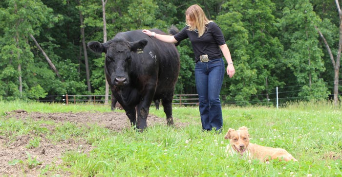 Lexi Koelling standing in the pasture with a cow and dog