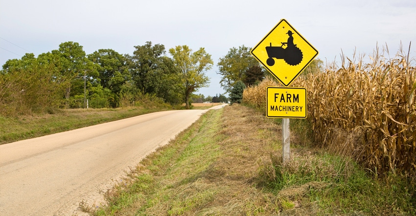 Caution farm machinery sign along side road and corn field