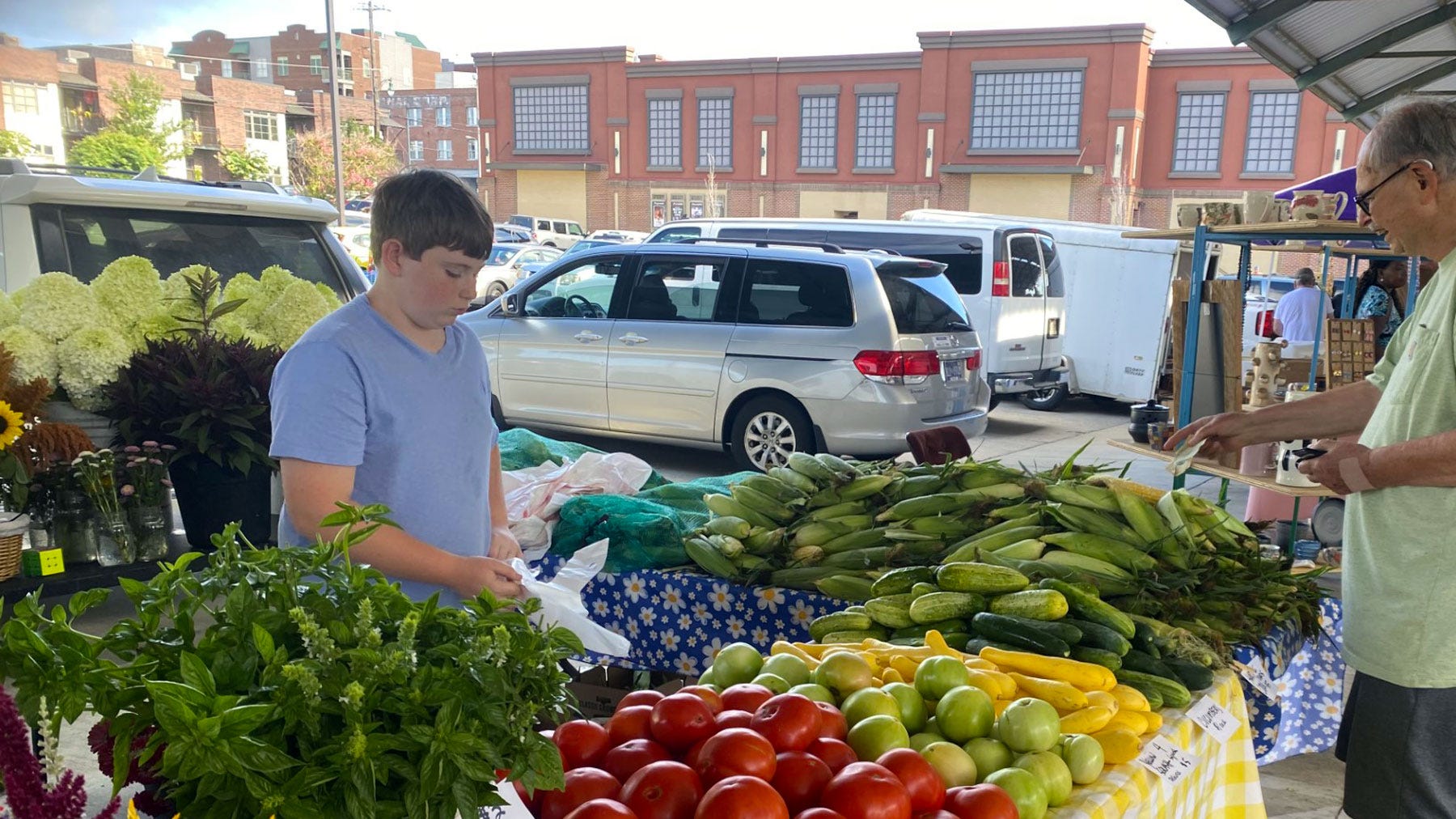 Boy working farmers market stand, bagging vegetables for a customer.