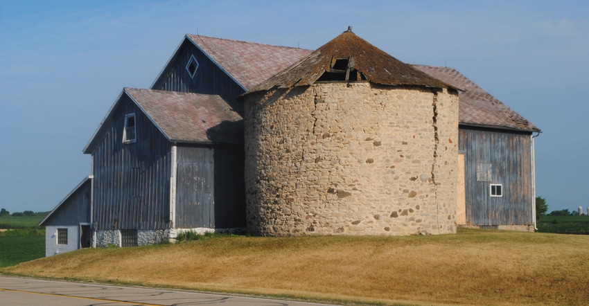 An old barn with a stone silo and roof that is torn and broken