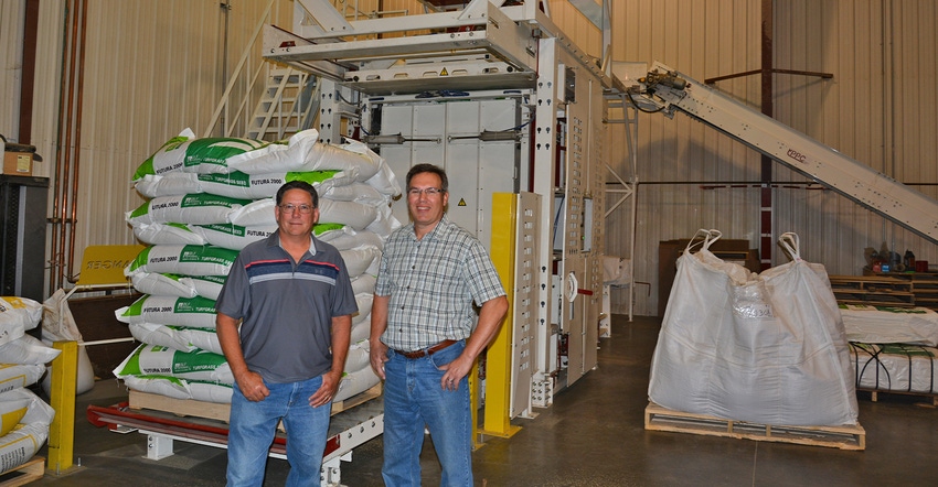 Milo Ravndalen (left) and Brent Benike are standing in front of a robotic palletizer at the Northern Excellence seed conditio