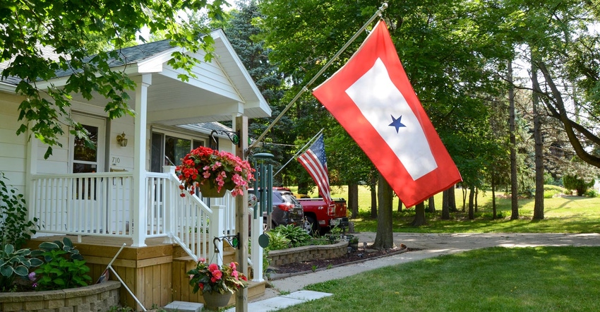 An American flag and a Blue Star flag flying high on the side of a white farmhouse