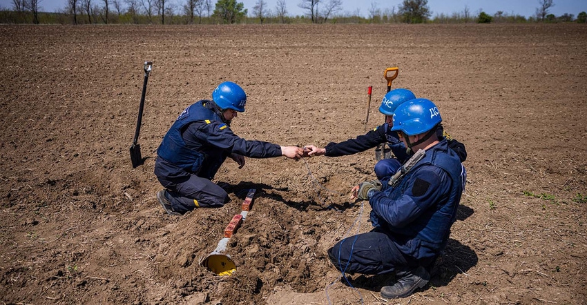 Members of a demining team of the State Emergency Service of Ukraine work to destroy an unexploded missile in a farm field be