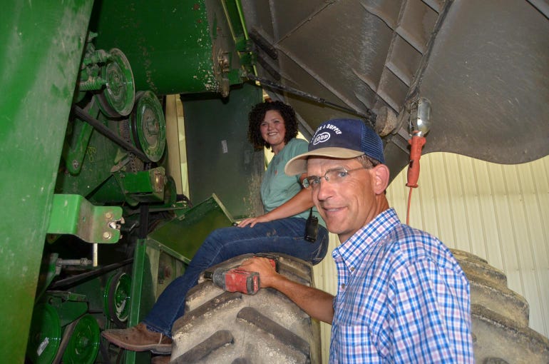 A young lady sitting on a tractor tire while she and her father work in the shop