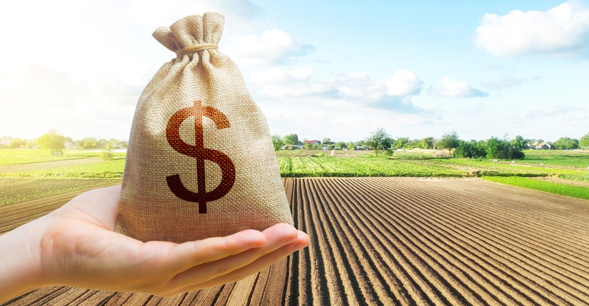 hand holding bag of money with farm in background