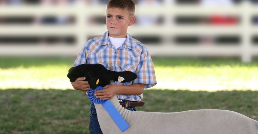 Young boy holding blue ribbon with winning goat