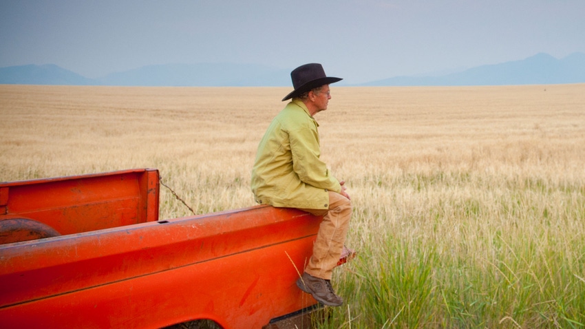farmer sitting on back of pickup truck looking off into the distance