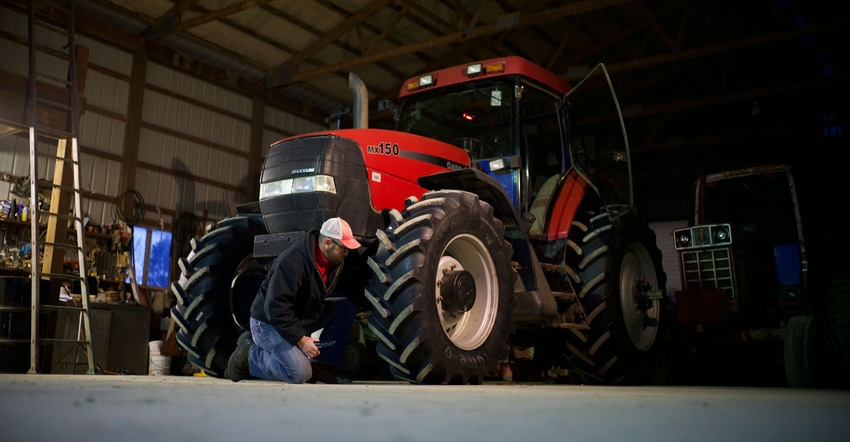 A farmer works on winter tire care of a tractor stored in a machine shed