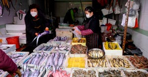 A seafood vendor wearing a mask and gloves talking to a customer at a wet market in China