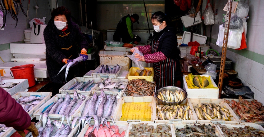 A seafood vendor wearing a mask and gloves talking to a customer at a wet market in China A seafood vendor wearing a mask and gloves talking to a customer at a wet market in China