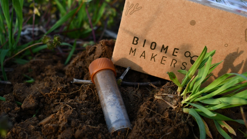 Soil test tube with orange lid, resting in fresh soil with Biome Makers box in the background.