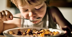 Child eating bowl of cereal and milk dripping off spoon.