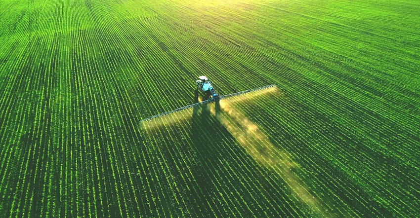 tractor spraying fertilizer on green field