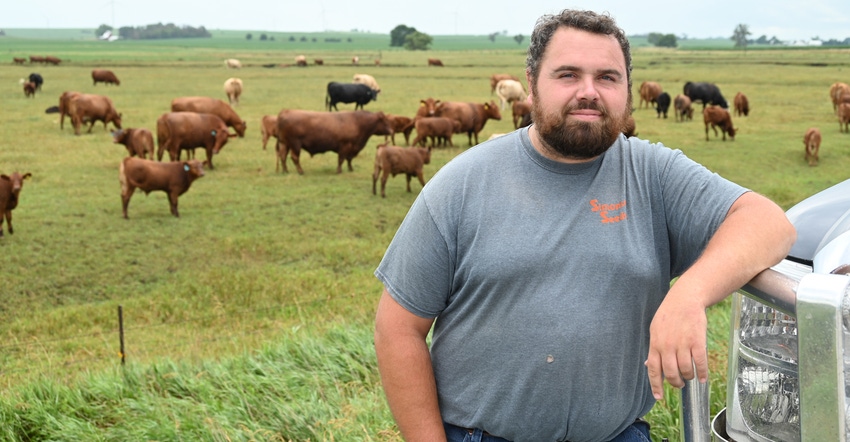 Adam Glienke’s standing in pasture with cattle behind him