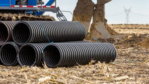 Black corrugated water drainage pipe in farm field and a tractor in the background