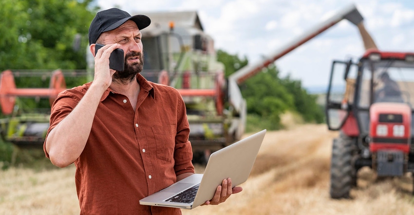 Farmer using smartphone in field with equipment in background