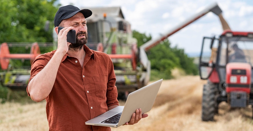 Farmer using smartphone in field with equipment in background Farmer using smartphone in field with equipment in background