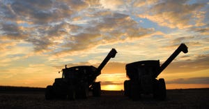 silhouette of 2 combines at sunset