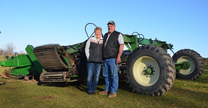 A man and woman stand in front of a tractor and pose for a photo
