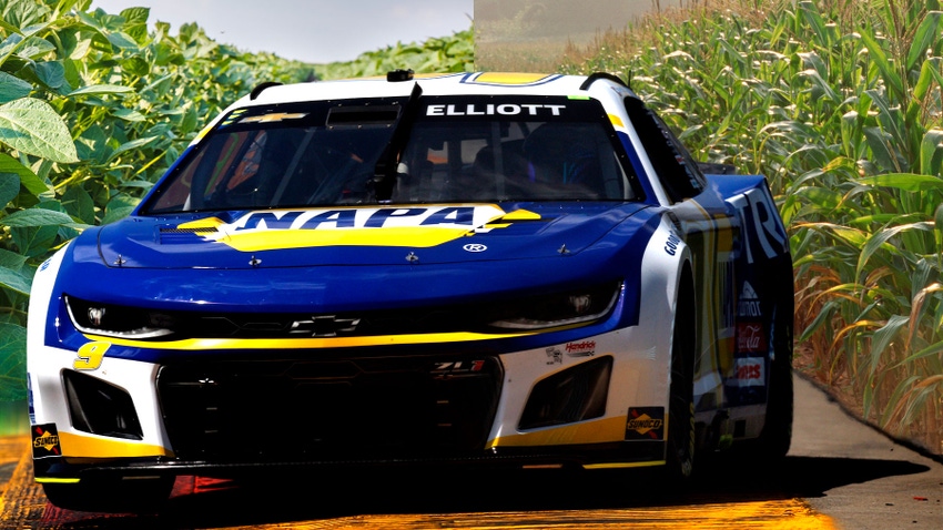 A race car with a background of a soybean field on the left and a corn field on the right