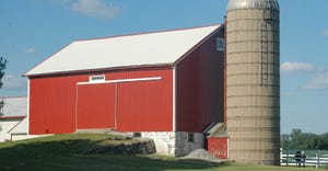 A red barn and grain bin with a white wooden fence