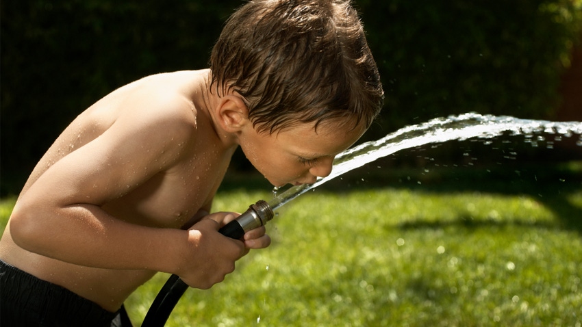 Boy drinking water from garden hose