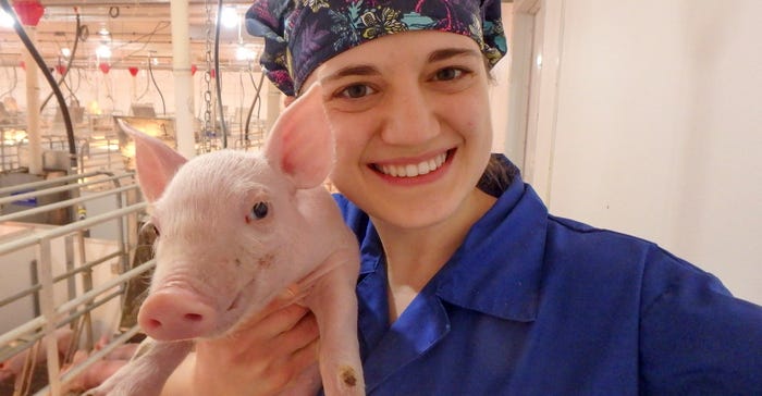 Janae smiles and holds a piglet