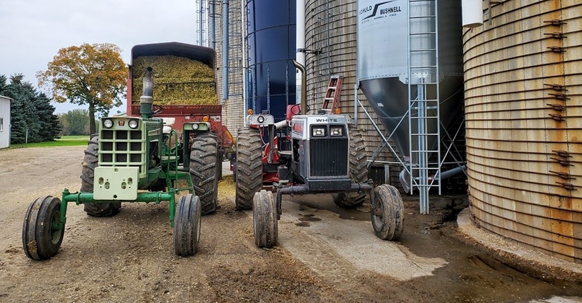 A tractor filled with corn silage next to silos