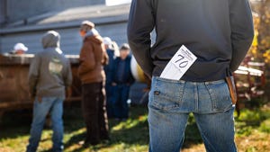 The back view of a man standing with his hands in his pockets and an auction number sticking out of his back pocket