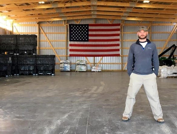 Adam Kramer standing in barn with american flag in the background