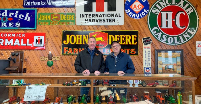 Father and son Doug and John Aylward standing in front of a collection of tractors in glass case