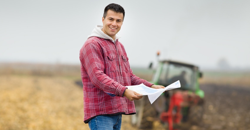 A farmer holds up paperwork in a field