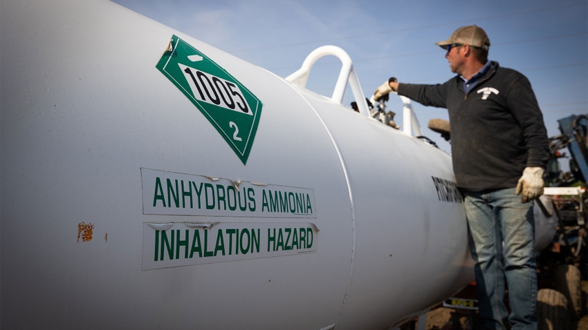 A man moving a valve on a large white tank containing anhydrous ammonia