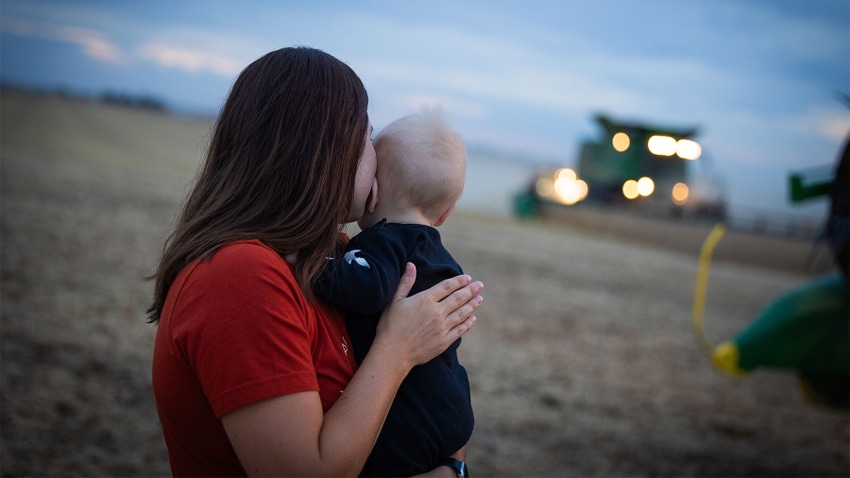  profile view of a young woman carrying a baby as they look behind towards the headlights of a combine