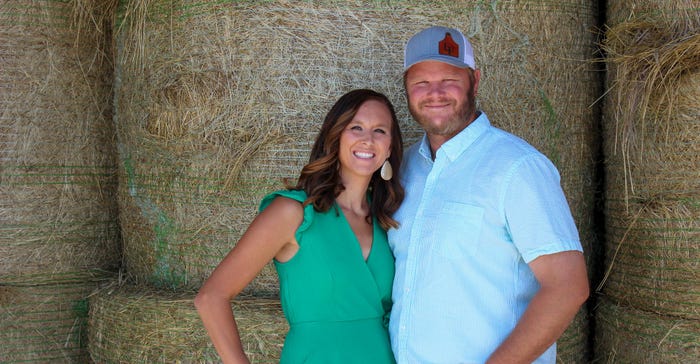 A man and a woman stand in front of bales of hay smiling for a photo