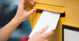 Close-up of hands inserting a white envelope into a yellow mailbox