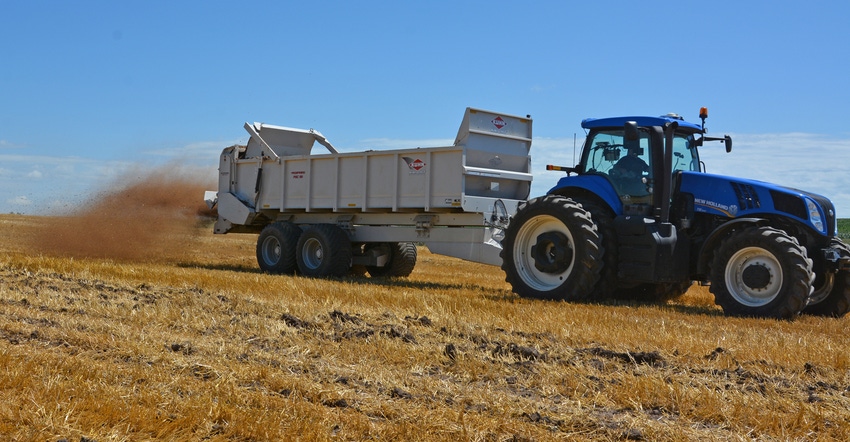 tractor and cart hauling and spreading manure across field tractor and cart hauling and spreading manure across field